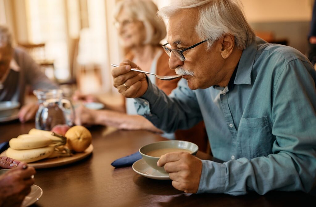 An older adult enjoys a meal with friends in the communal dining room of their assisted living community.