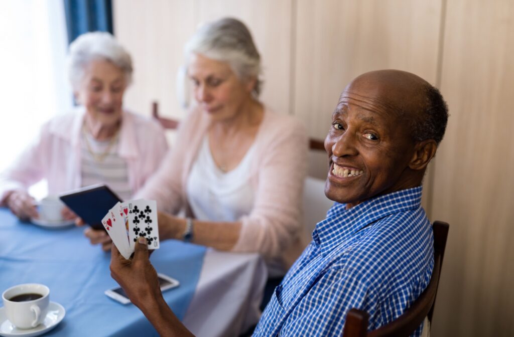 A happy older adult smiles while playing a card game with new friends in a shared assisted living community