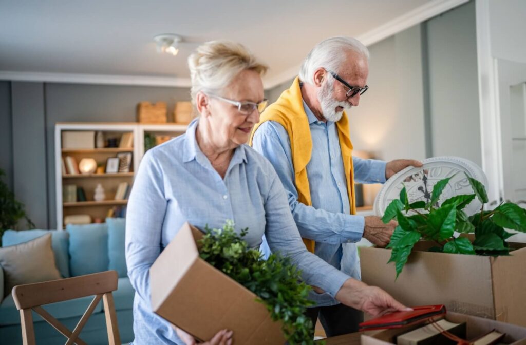 Two older adults carefully pack up a clock and some fake plants into boxes during a move to their new senior living home
