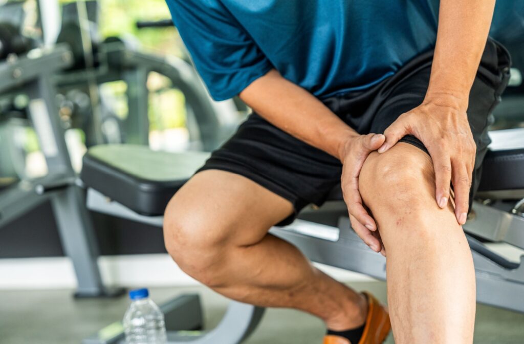 An older adult rubs their knee while sitting on an exercise bench during a fitness class in a gym